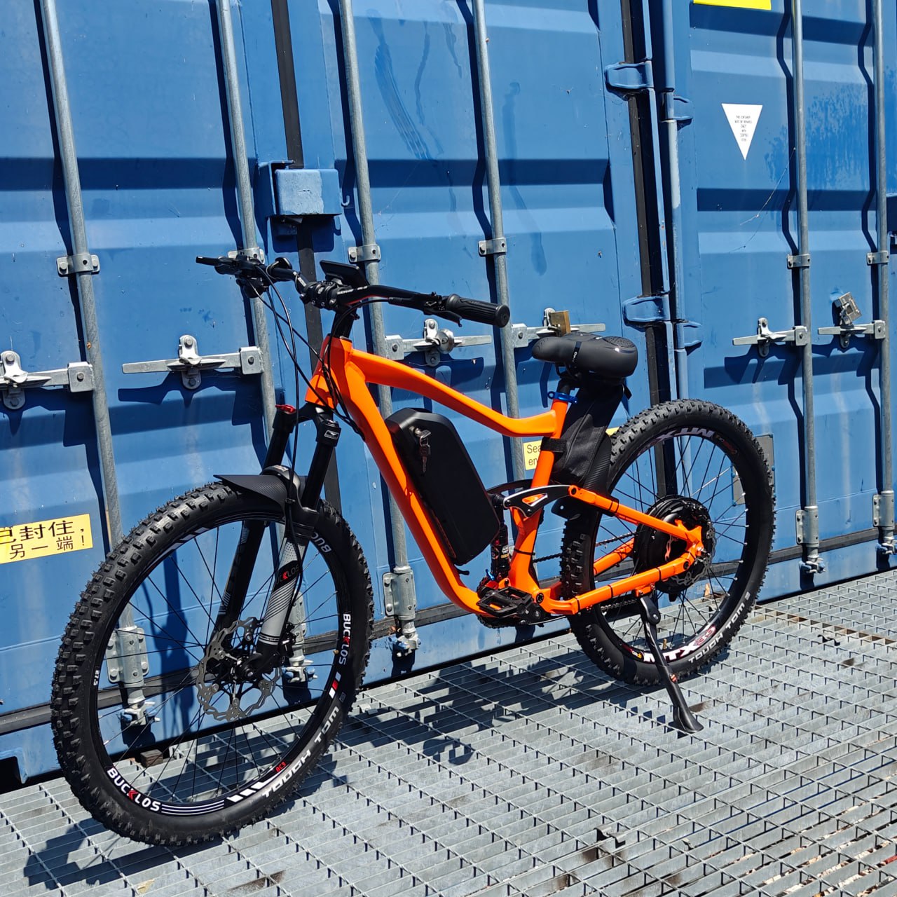 Orange bicycle leaning against a blue shipping container.
